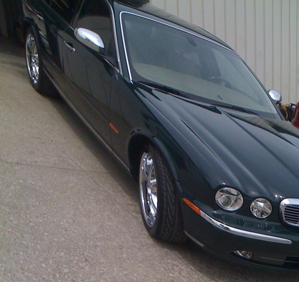 A dark green Jaguar sedan on chrome wheels, finished, outside the shop